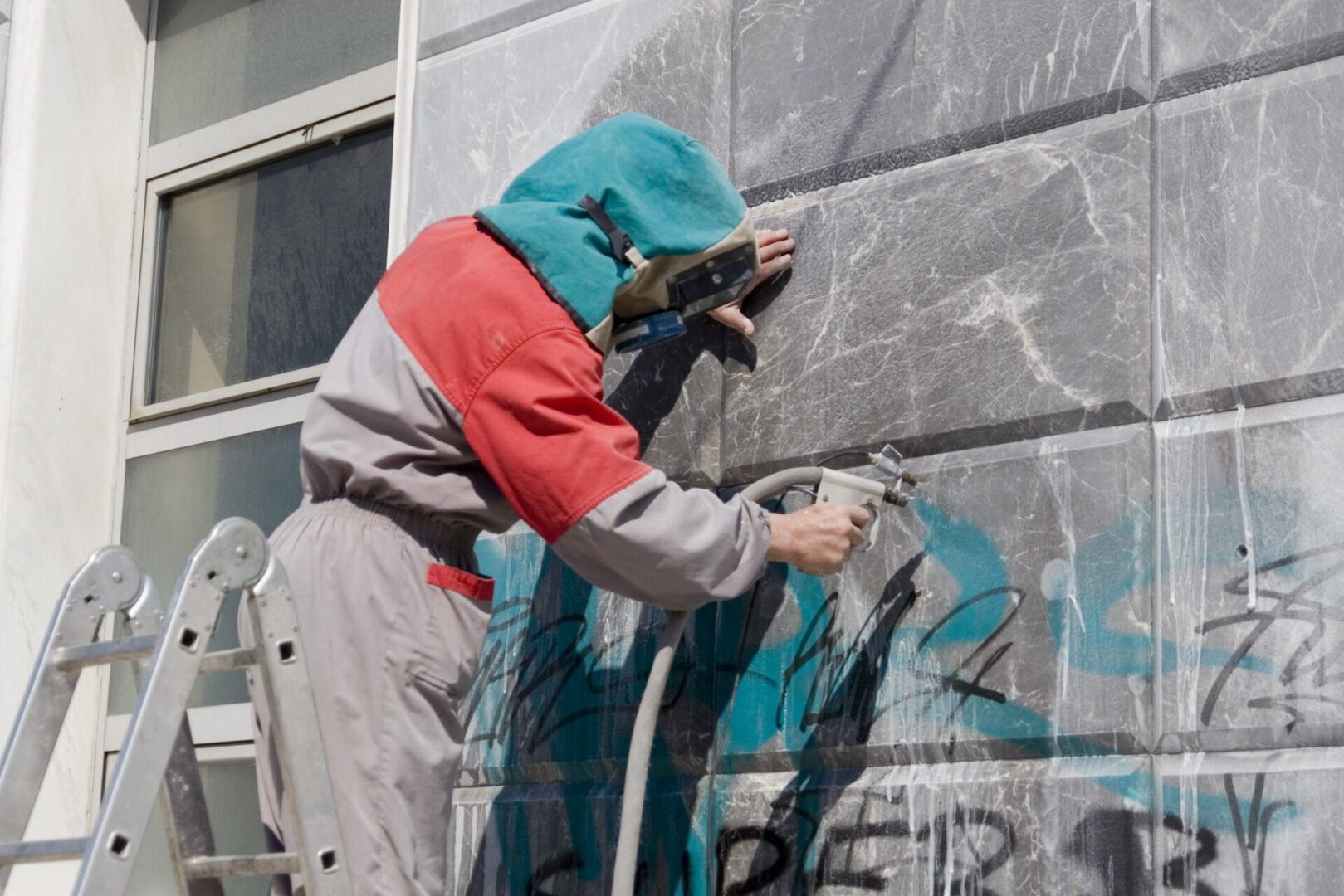 Worker removing graffiti from building wall